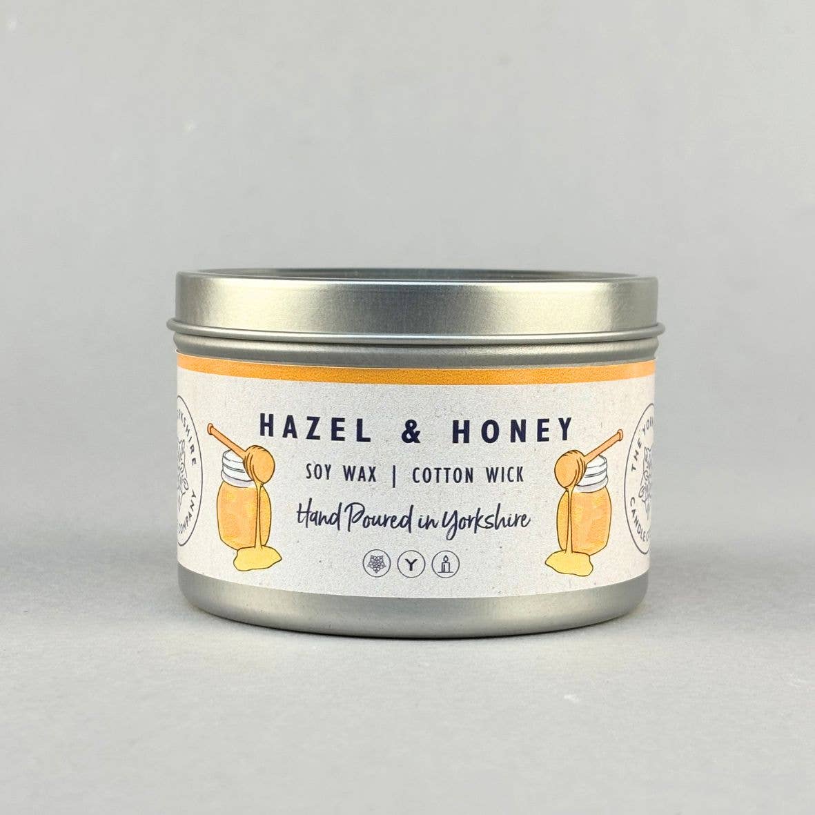 A silver metal tin candle with a white label reading 'HAZEL & HONEY' and 'SOY WAX | COTTON WICK', shown on a light gray background.