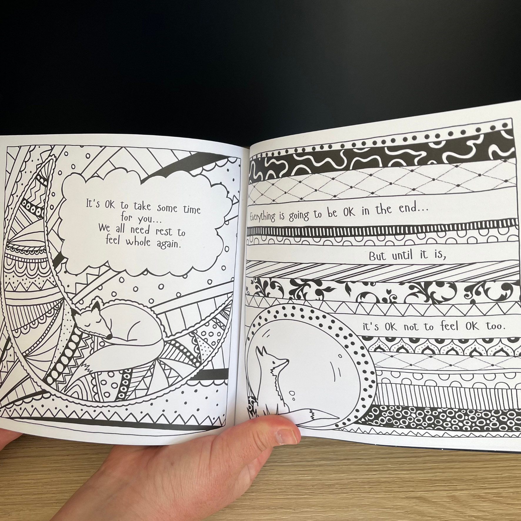 Open coloring book with black and white illustrations and text on a wooden surface.