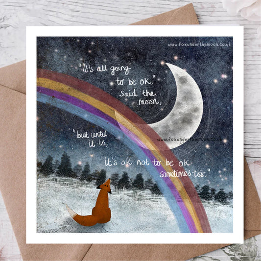 Card with a fox, rainbow, and moon illustration with motivational text on a wooden surface.
