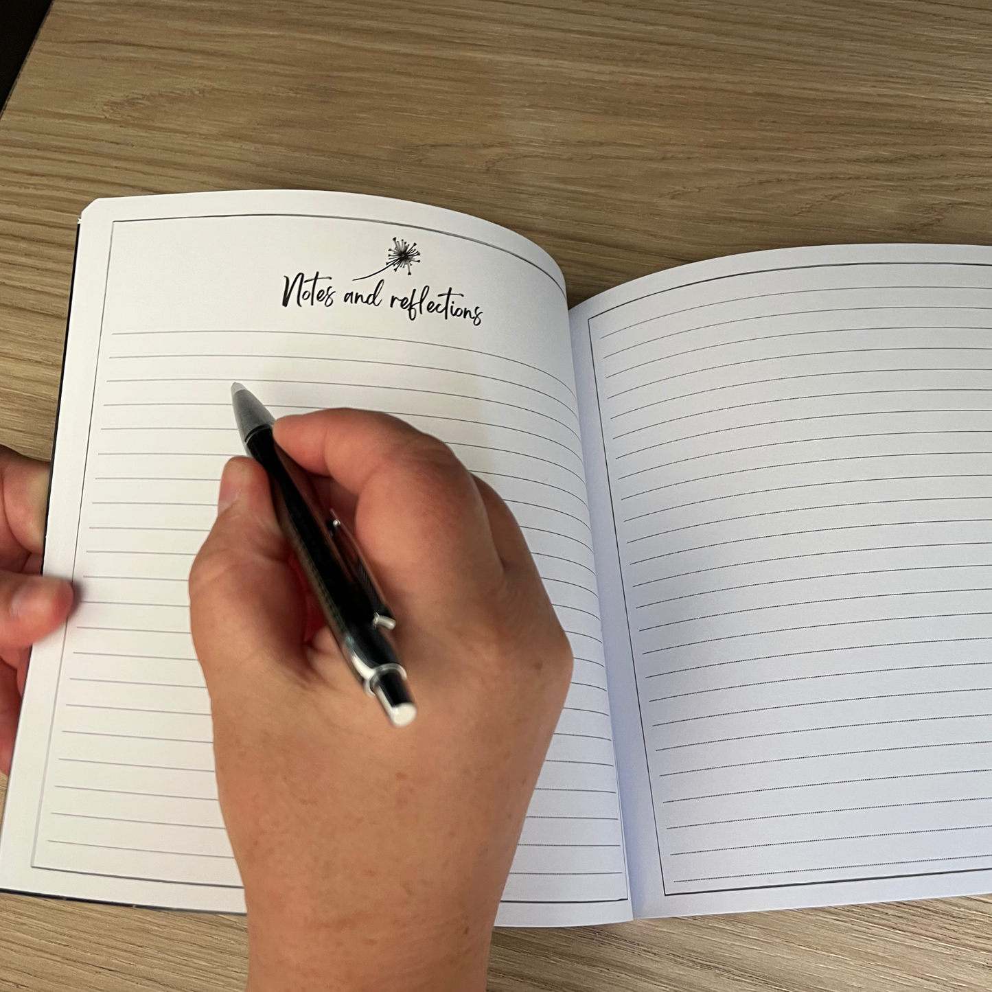 Hand holding a pen over an open notebook with lined pages on a wooden surface