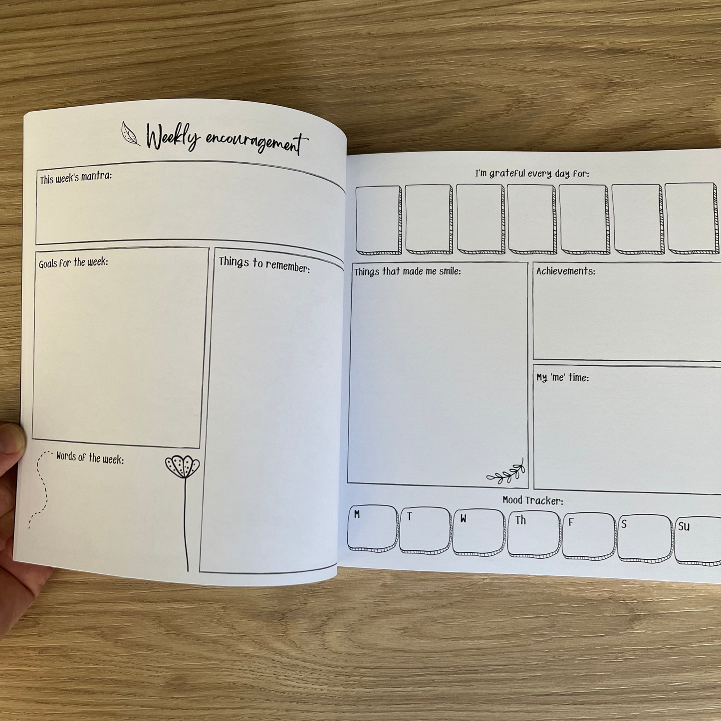 Open planner with weekly encouragement and mood tracker pages on a wooden surface