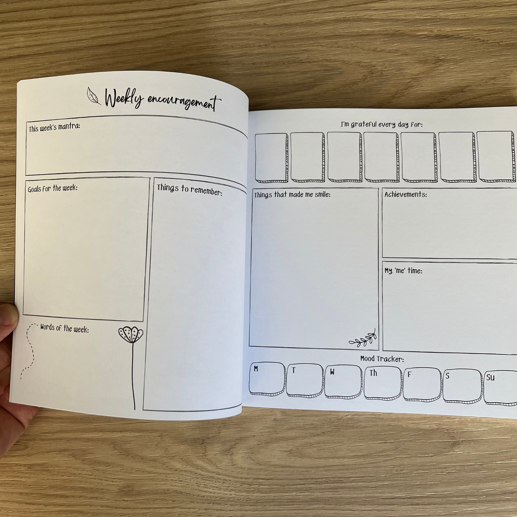 Open planner with weekly encouragement and mood tracker pages on a wooden surface