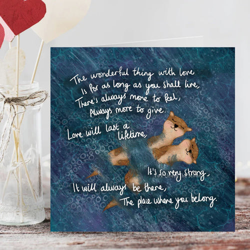 Card with two squirrels and a romantic quote on a blue background, placed on a wooden surface.