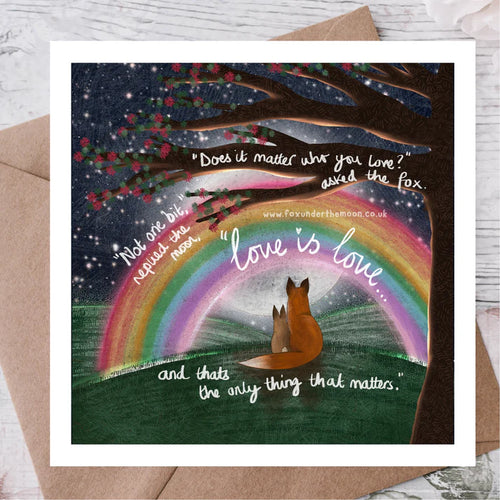 Card with foxes under a rainbow and romantic quote, placed on a wooden surface.