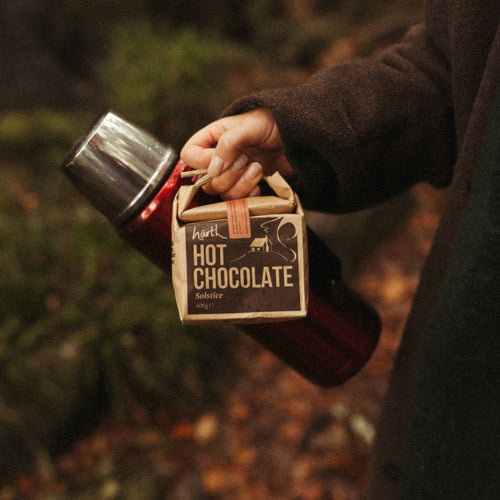 Person holding a container of hot chocolate in a forest setting