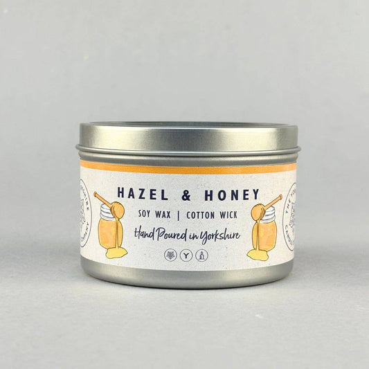 A silver metal tin candle with a white label reading 'HAZEL & HONEY' and 'SOY WAX | COTTON WICK', shown on a light gray background.