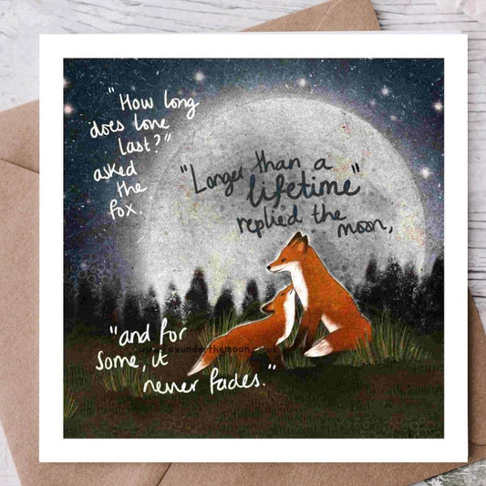 Greeting card with fox and moon illustration and romantic quote on a wooden surface.