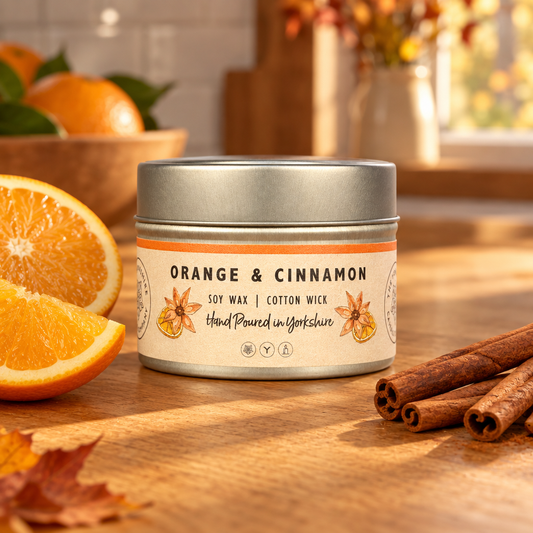 Orange & Cinnamon candle tin by The Yorkshire Candle Company beside orange slices and cinnamon sticks on a kitchen table