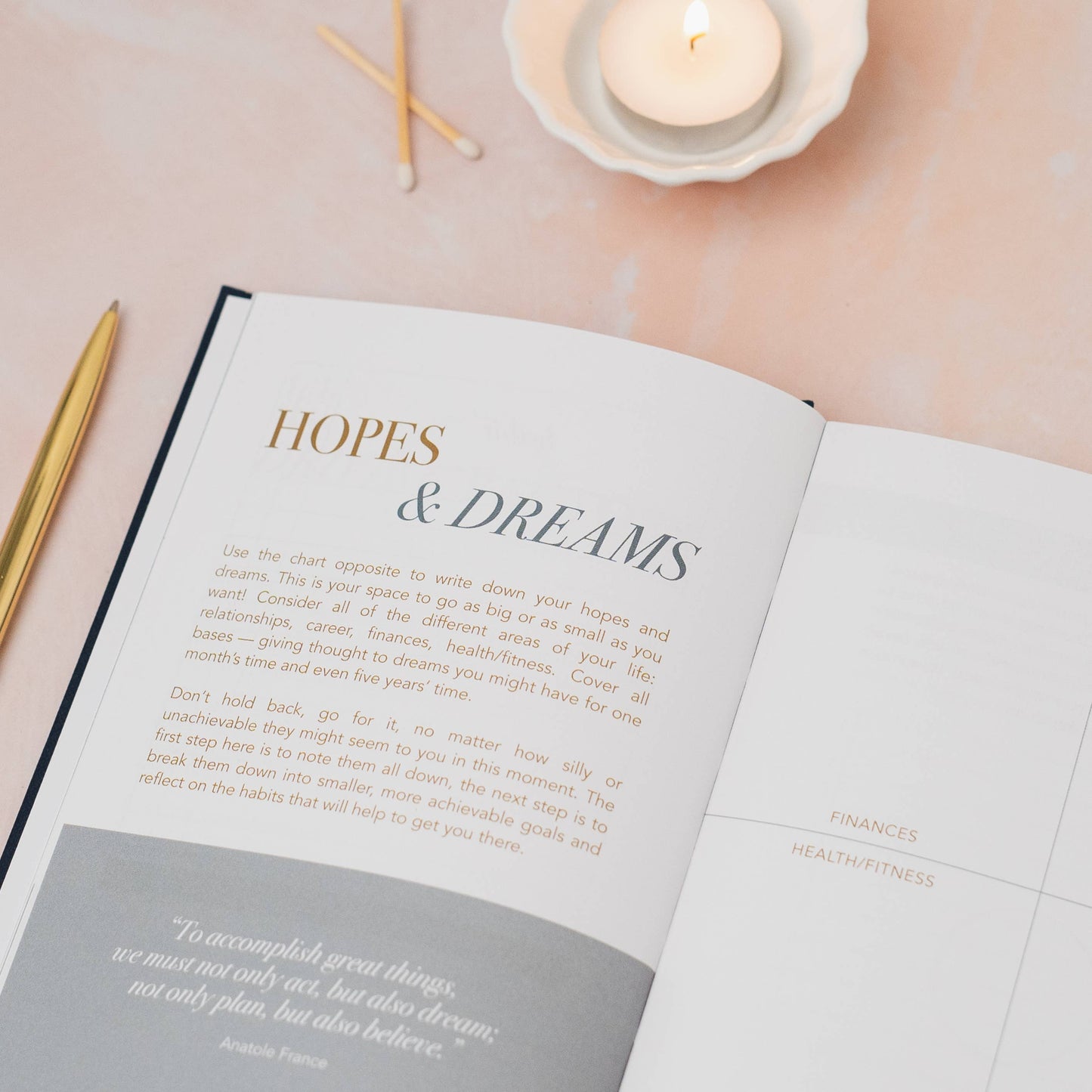 Open book titled 'Hopes & Dreams' on a light surface with candles and pens.