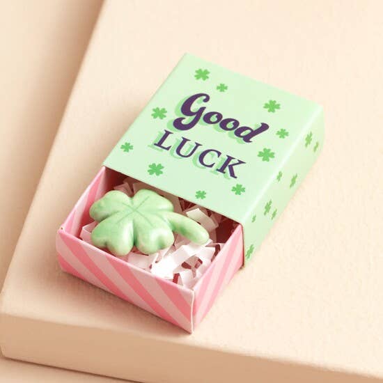 Small box with 'Good Luck' text and green four-leaf clover-shaped token on a beige background