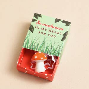 Mushroom-shaped gift in a decorative box with green grass design and text on a beige background