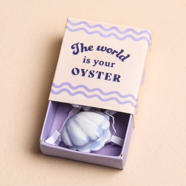 Clam shell shaped token in a box with 'The world is your oyster' text on a beige background