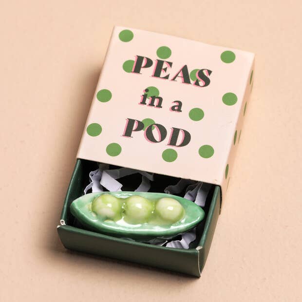 Decorative figurine with 'Peas in a Pod' packaging on a beige background