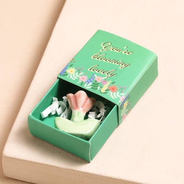 Green box with a pink flower-shaped item and floral design on a beige background