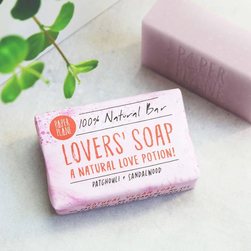 Bar of 'Lovers' Soap' with packaging on a light surface, featuring green leaves in the background.
