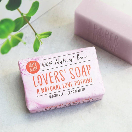 Bar of 'Lovers' Soap' with packaging on a light surface, featuring green leaves in the background.