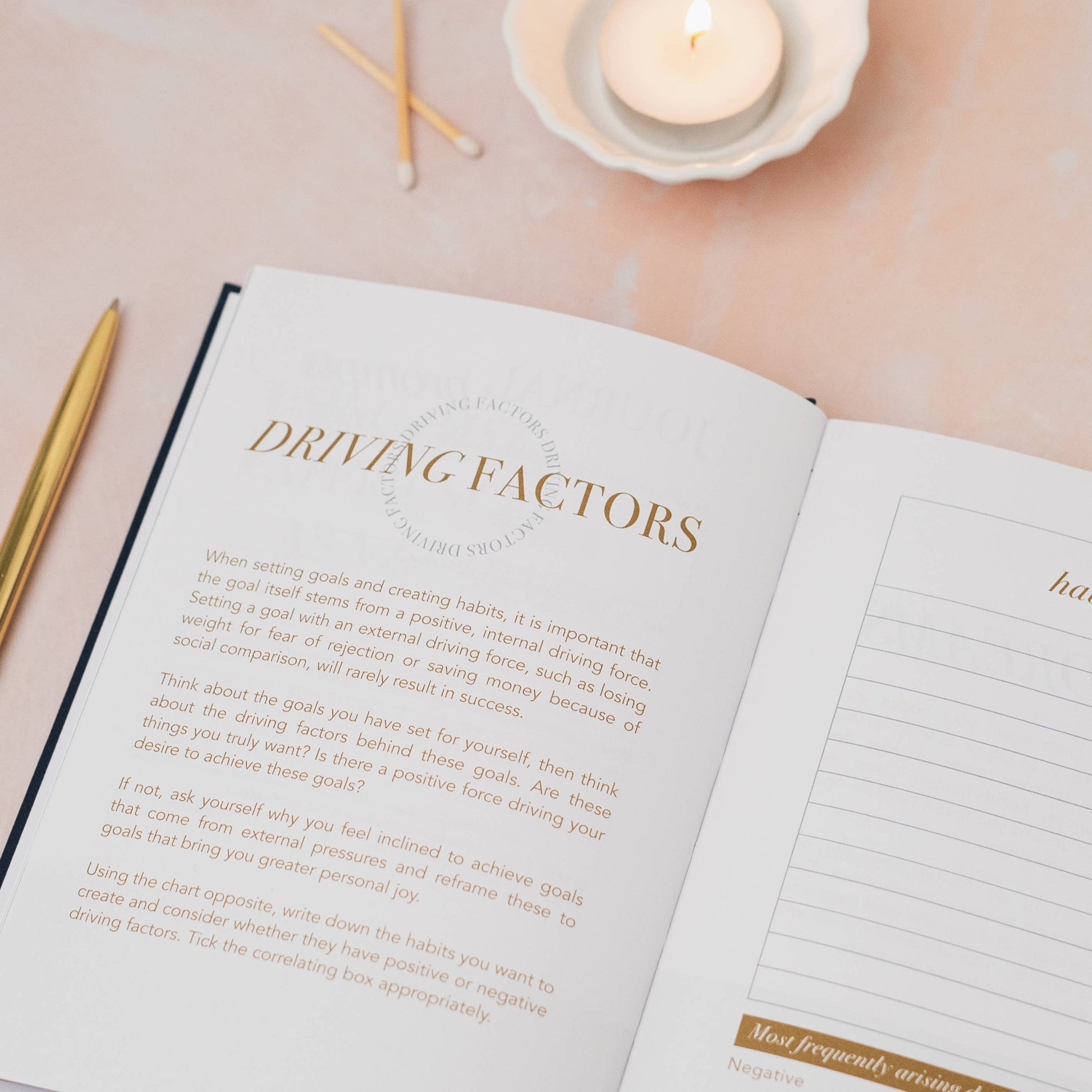 Open book with 'DRIVING FACTORS' chapter on a soft pink surface with candles and pencils.