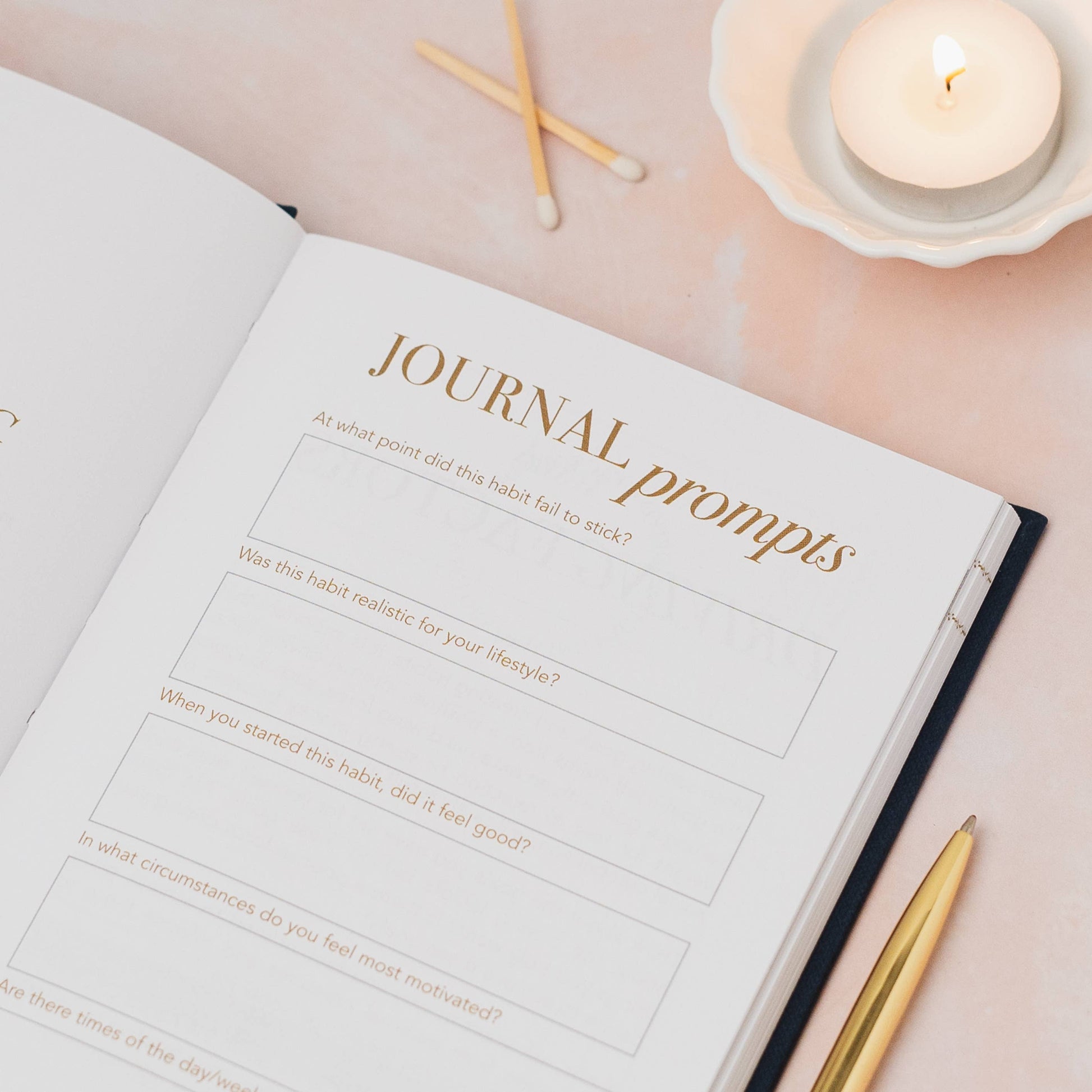 Journal with 'Journal prompts' on a light pink surface with a candle and pen.