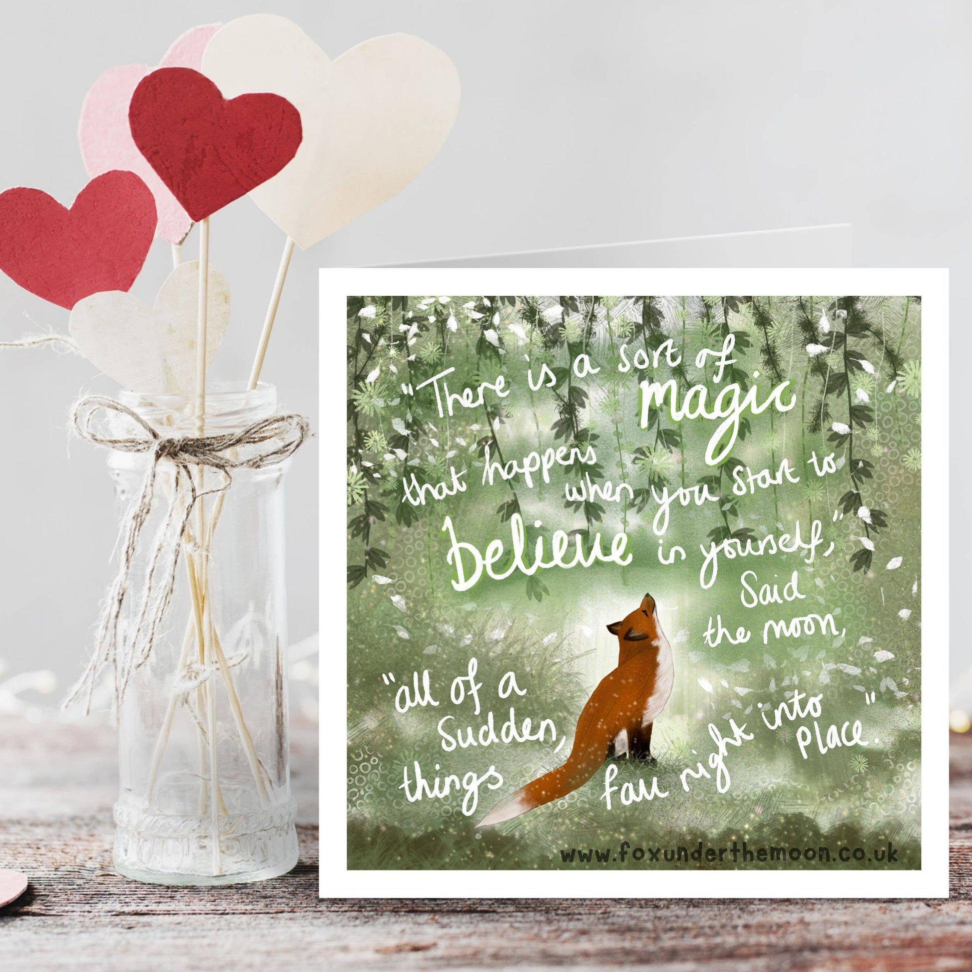 Decorative setup with a jar of hearts and a fox illustration on a wooden surface.