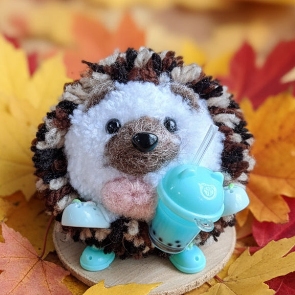 Plush toy hedgehog with a blue bobo tea cup and crocs on a wooden surface
