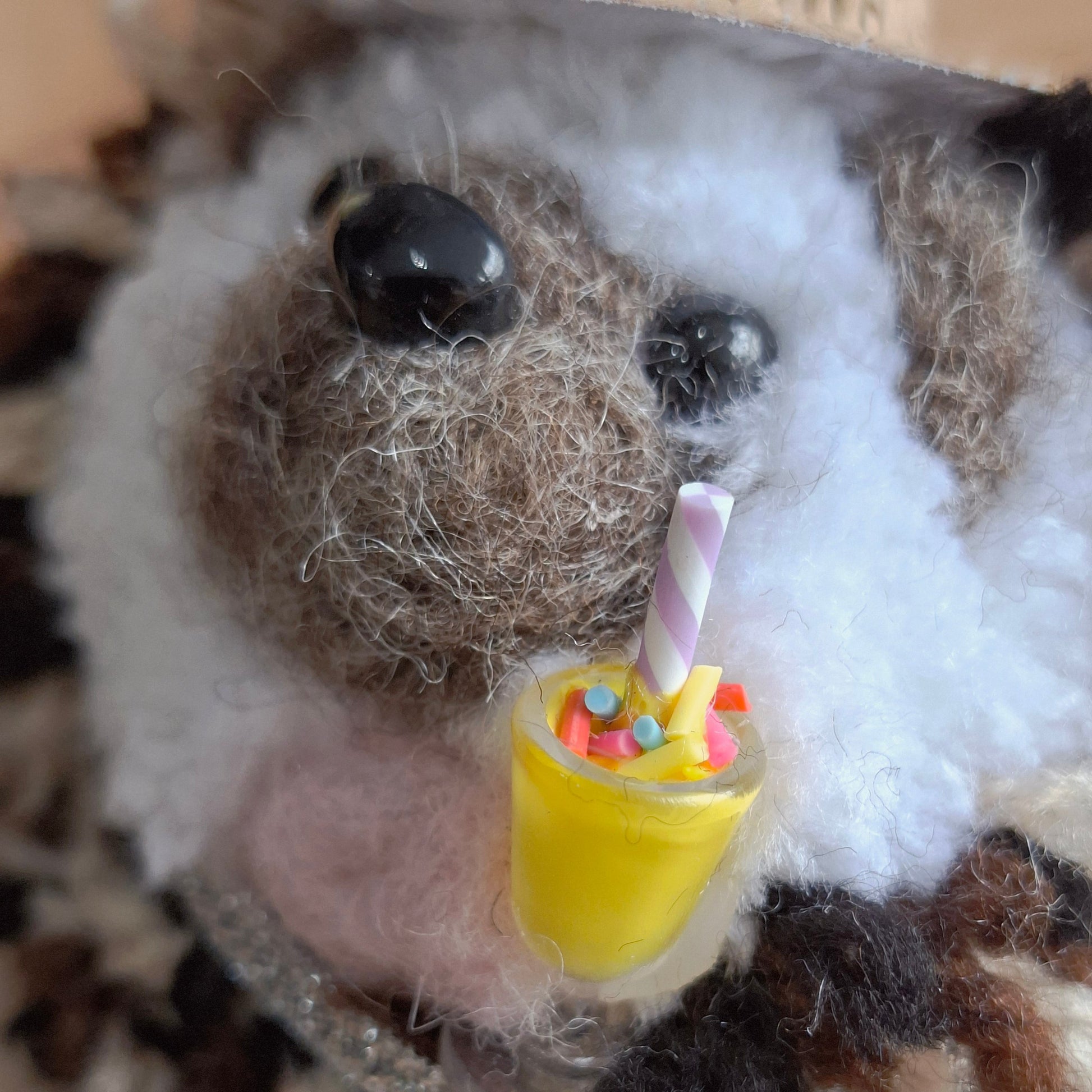 Close-up of a woollen hedgehog ornament with a small yellow milkshake in its paw