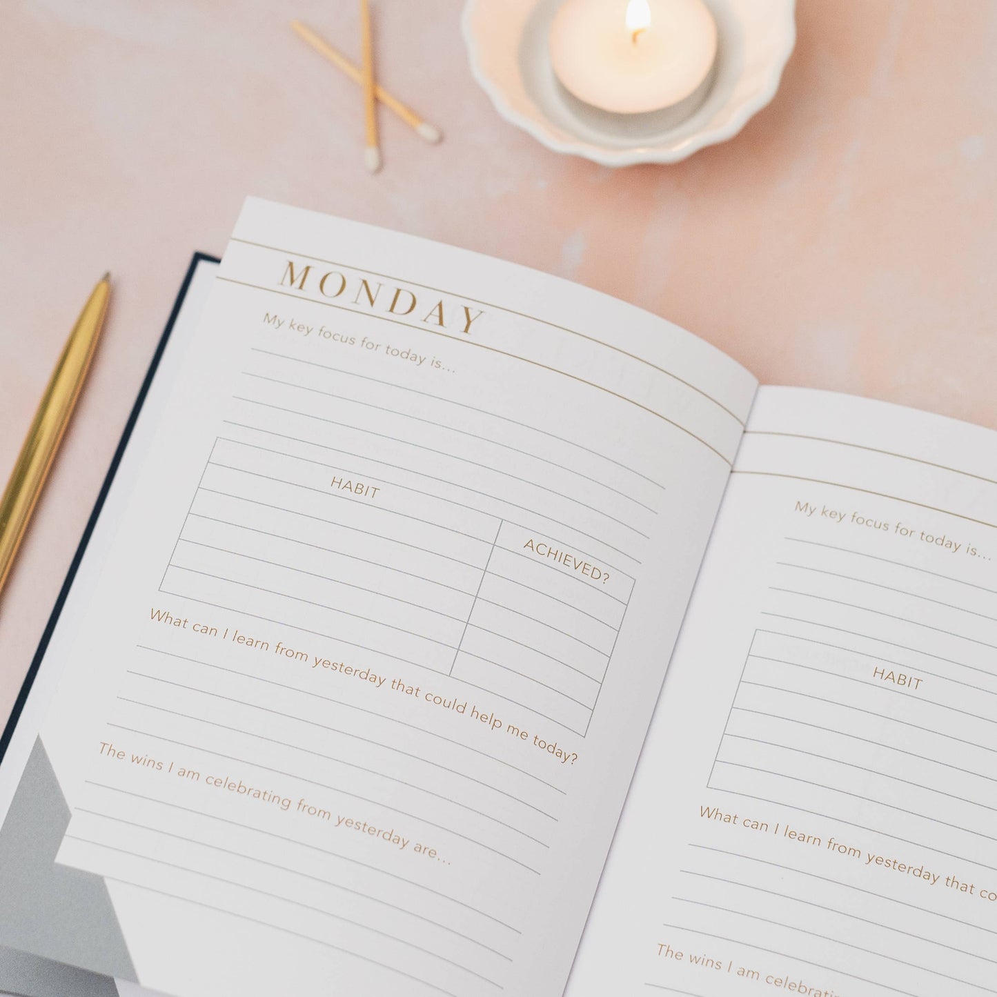 Open planner with daily layout on a soft pink surface with candles and pencils.