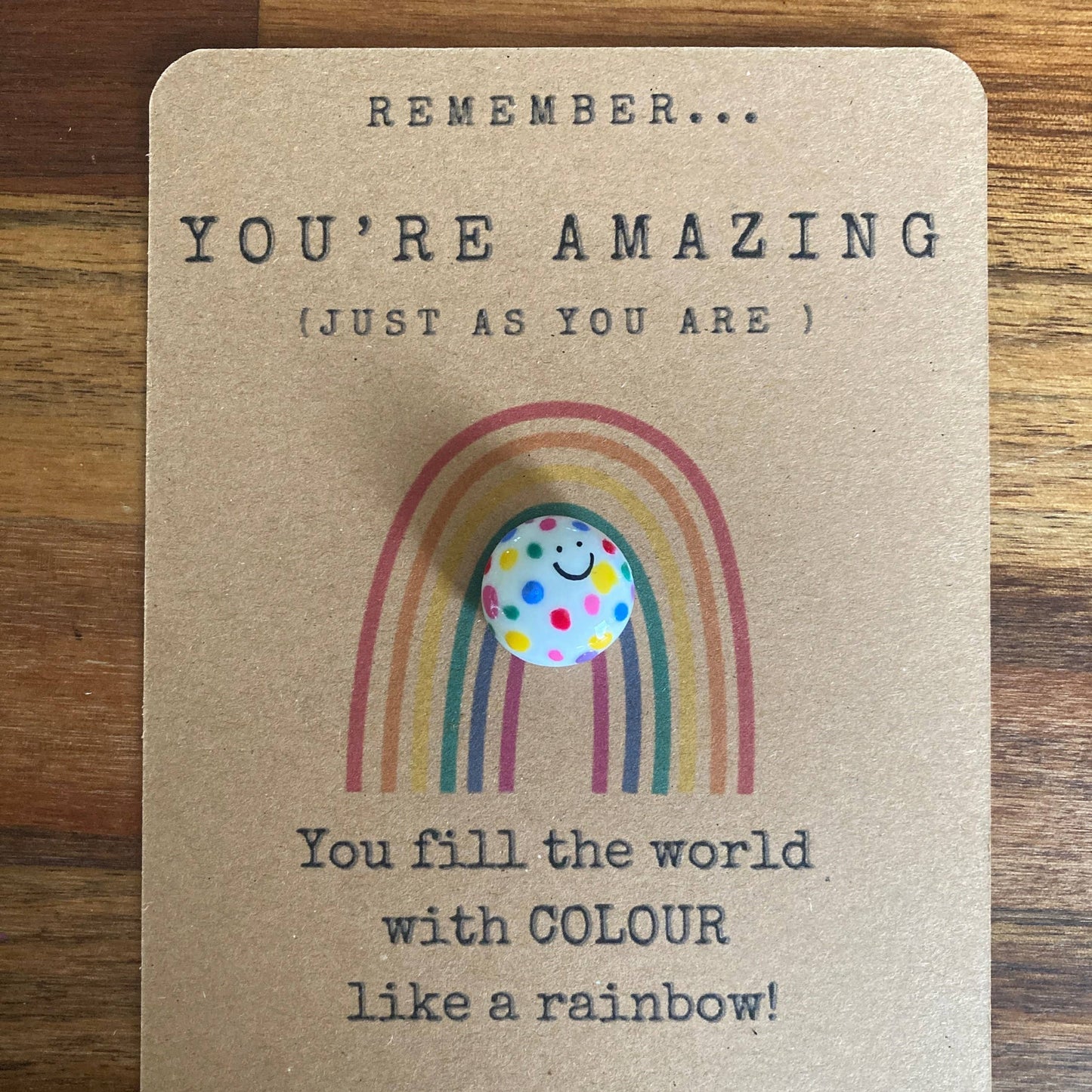 Card with rainbow design and polka dot charm on a wooden surface