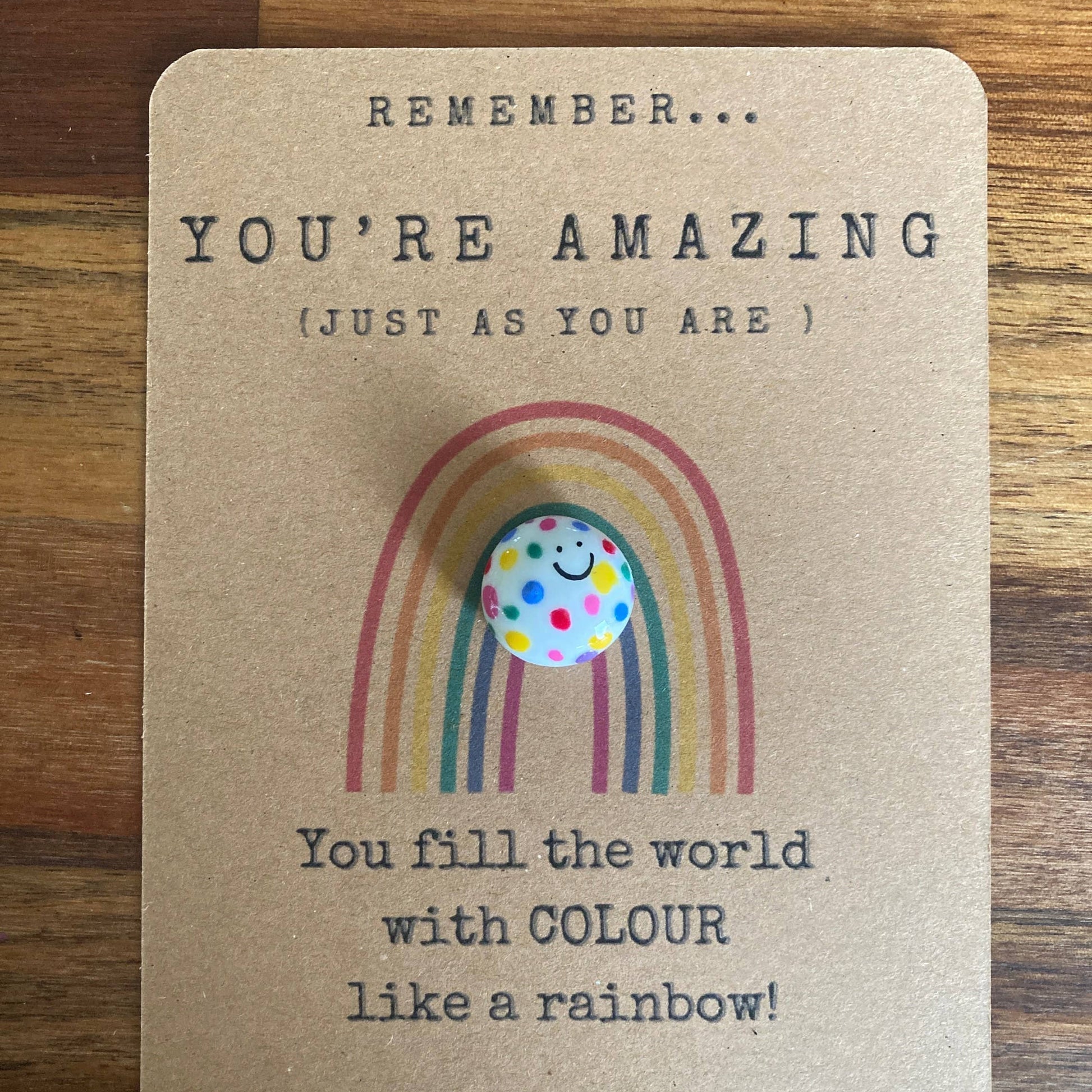 Card with rainbow design and polka dot charm on a wooden surface