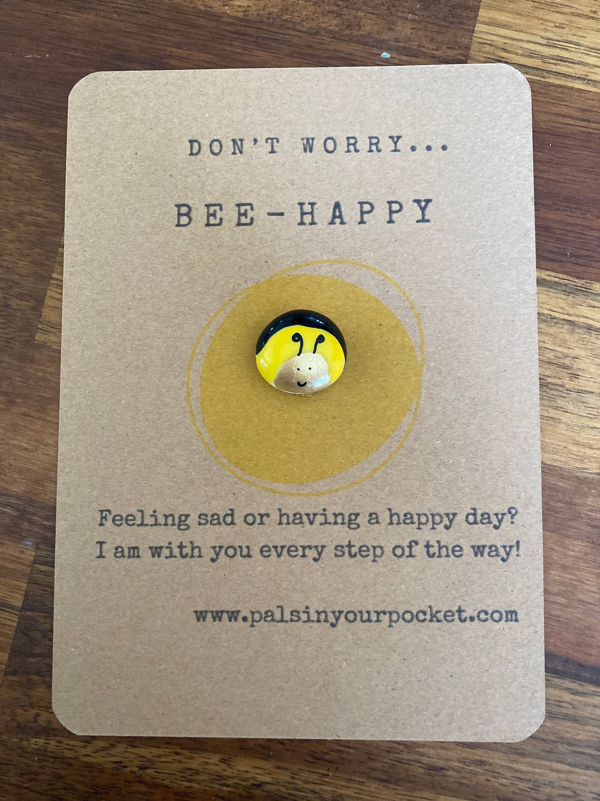 Card with a bee-themed button and text on a wooden surface