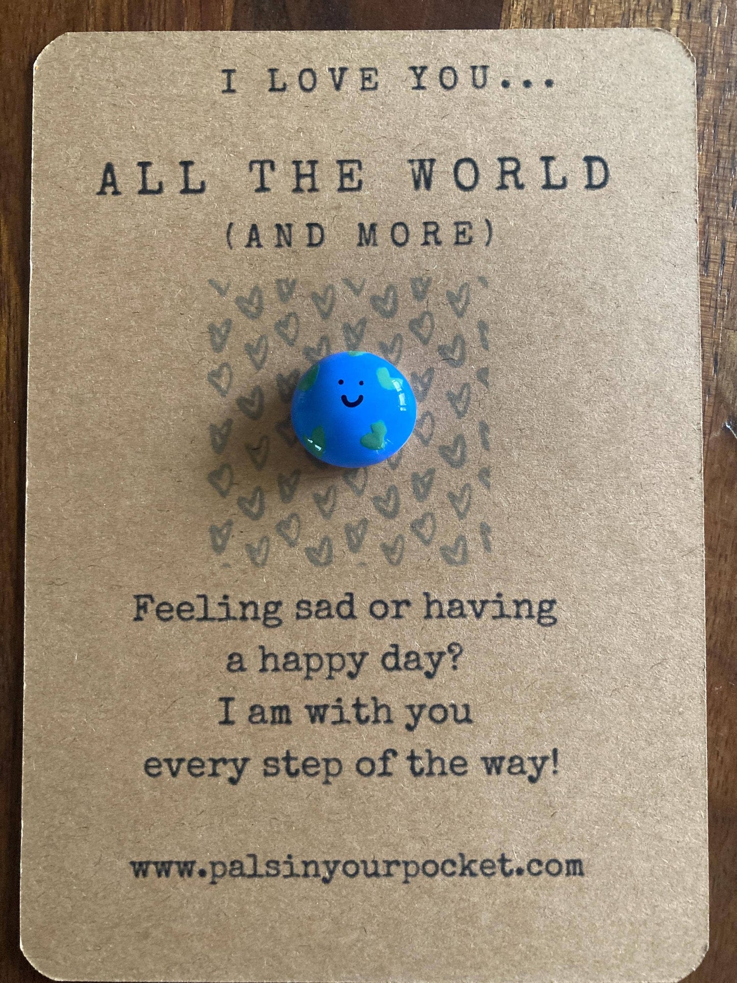 Card with a blue Earth-shaped charm and motivational text on a wooden surface