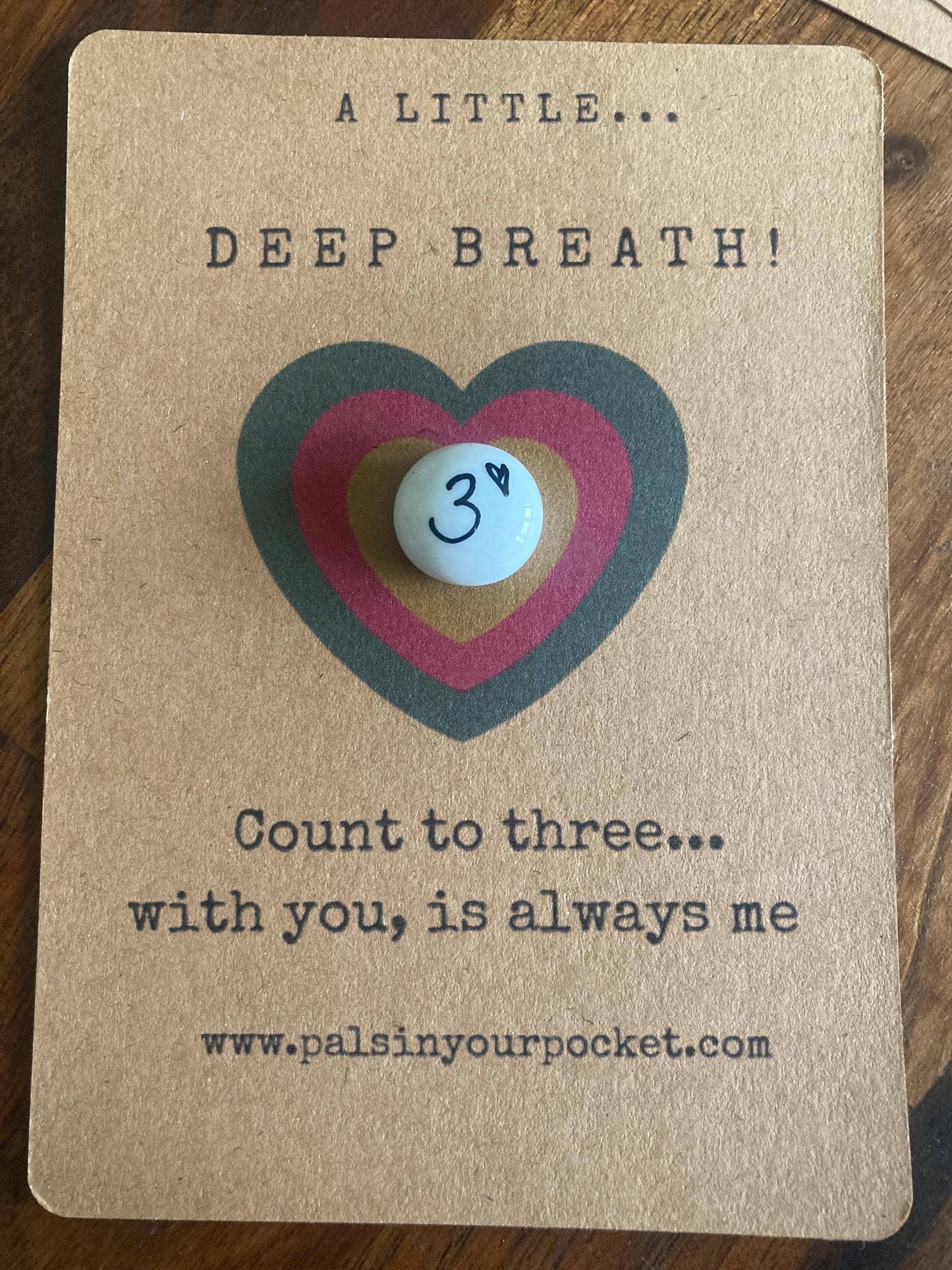 Card with a heart-shaped button and text on a wooden surface