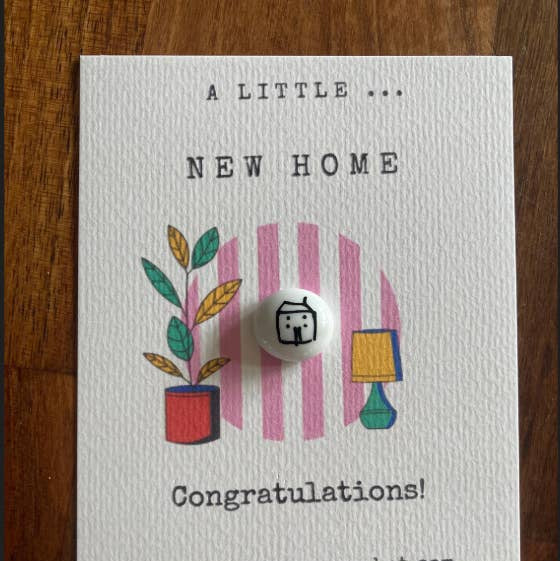 Greeting card with 'A Little New Home' text and illustrations on a wooden surface