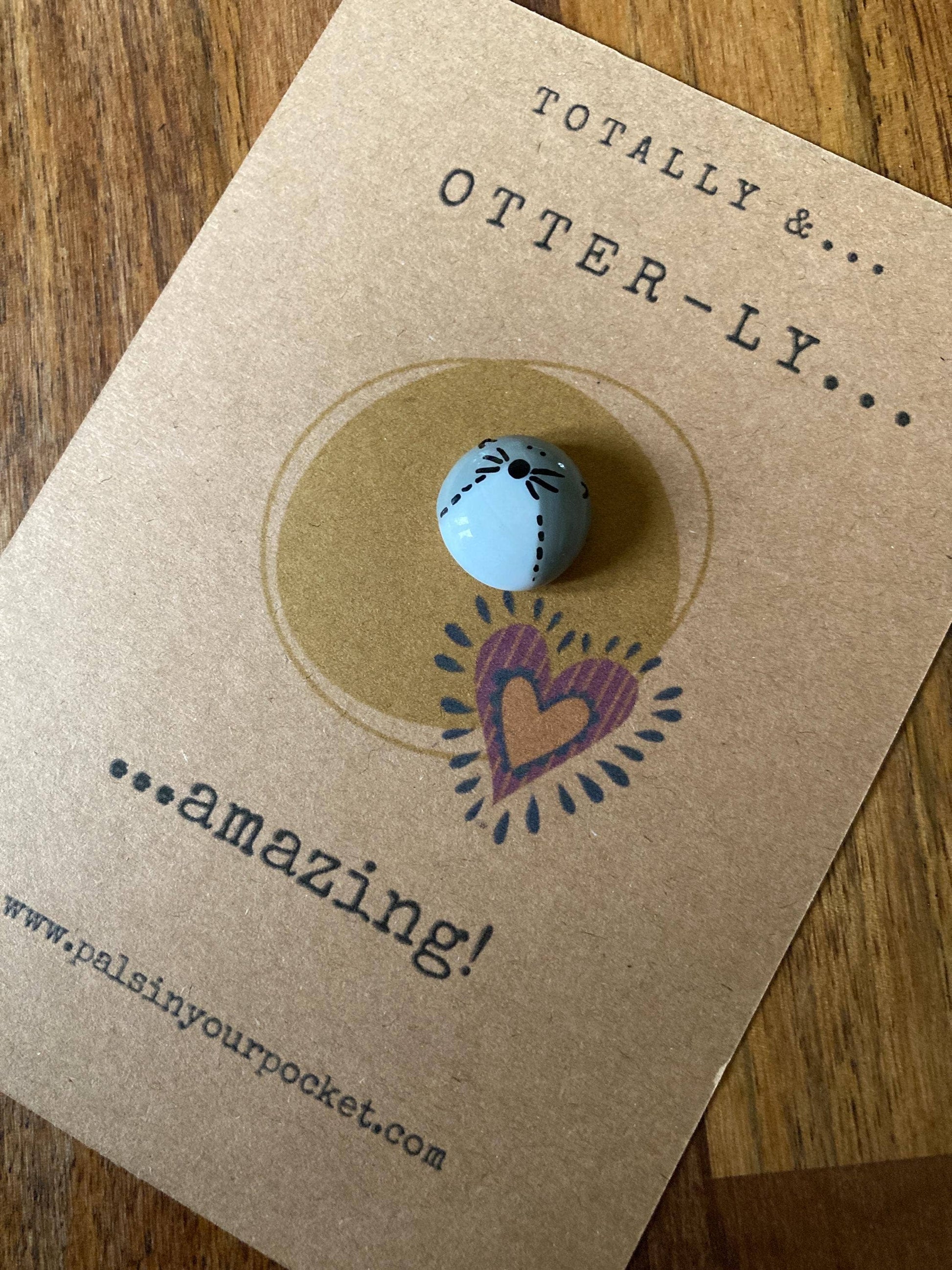 Otter pebble with heart design on a brown card with text 