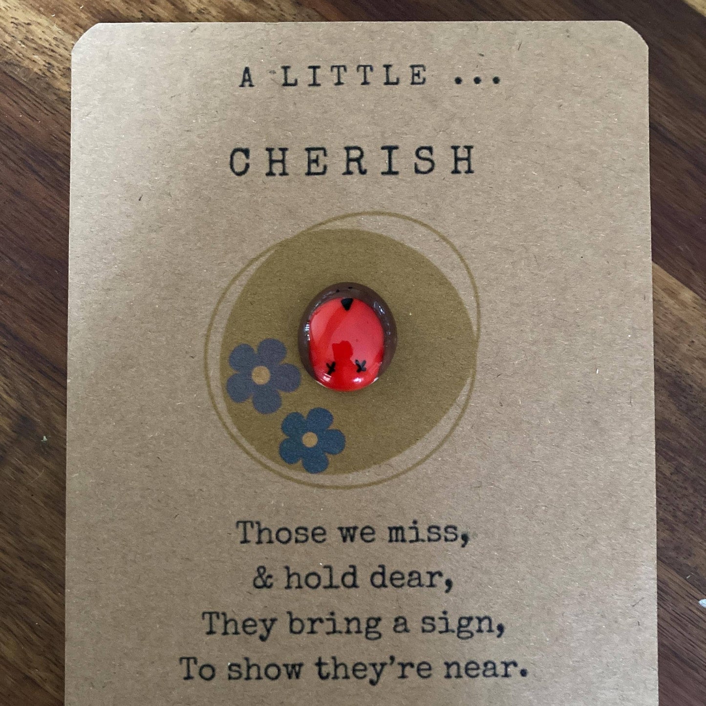 Card with a red and brown pebble and blue flowers on a brown background with text.