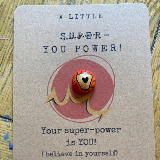 Card with a small red and gold pebble on a textured surface