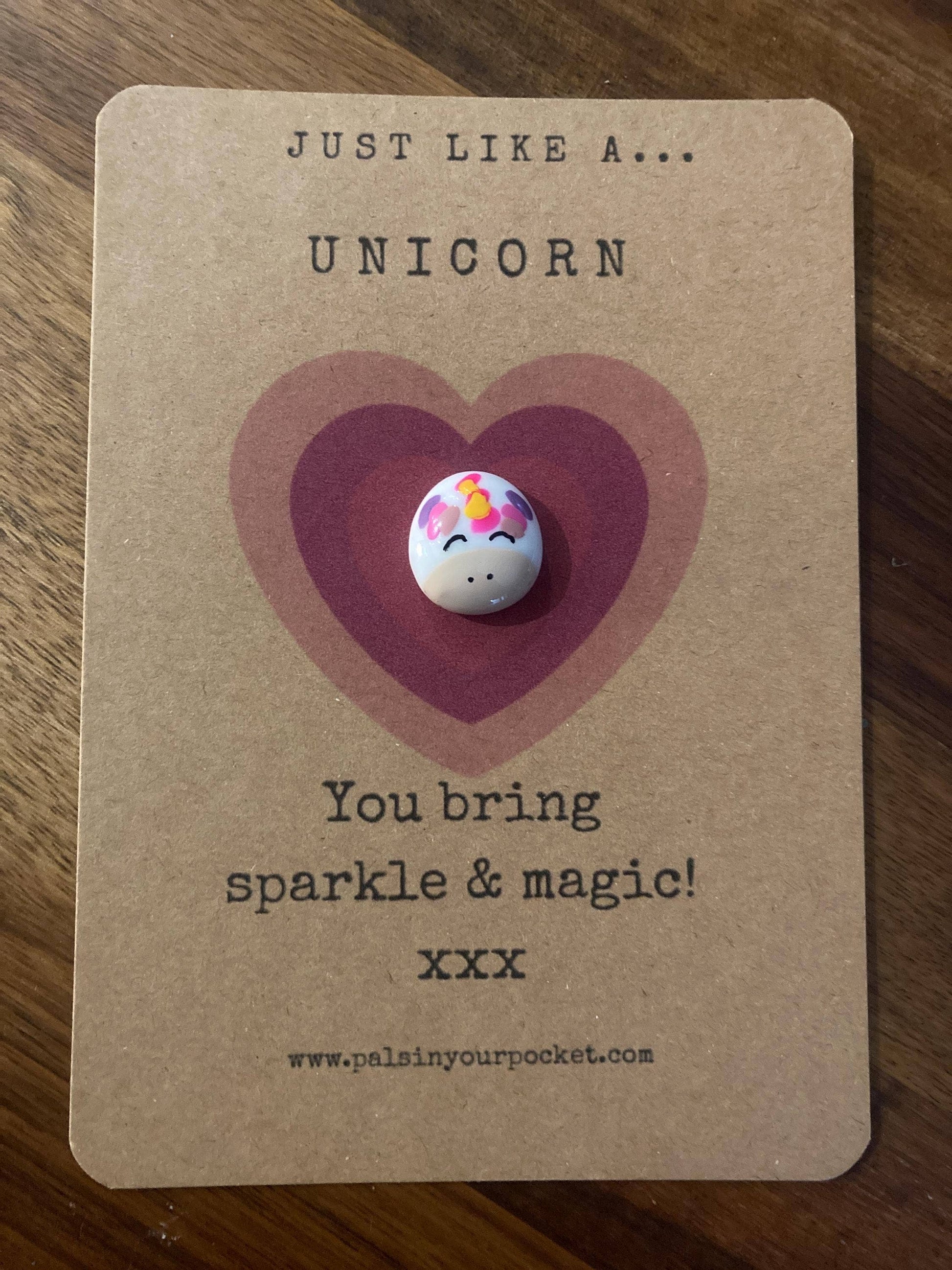 Unicorn-shaped charm on a brown card with text and a heart design