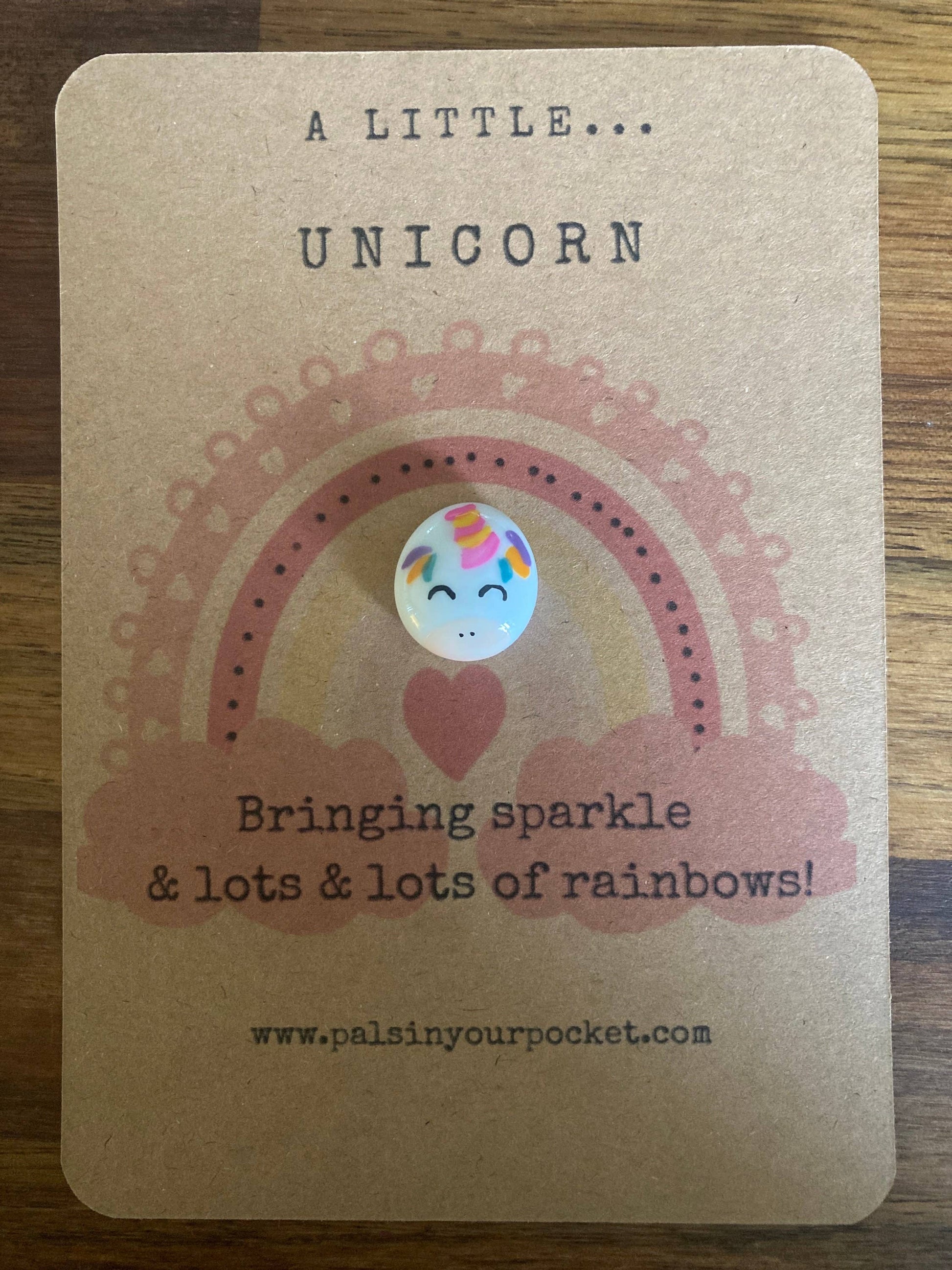 Card with a unicorn button and rainbow design on a wooden surface