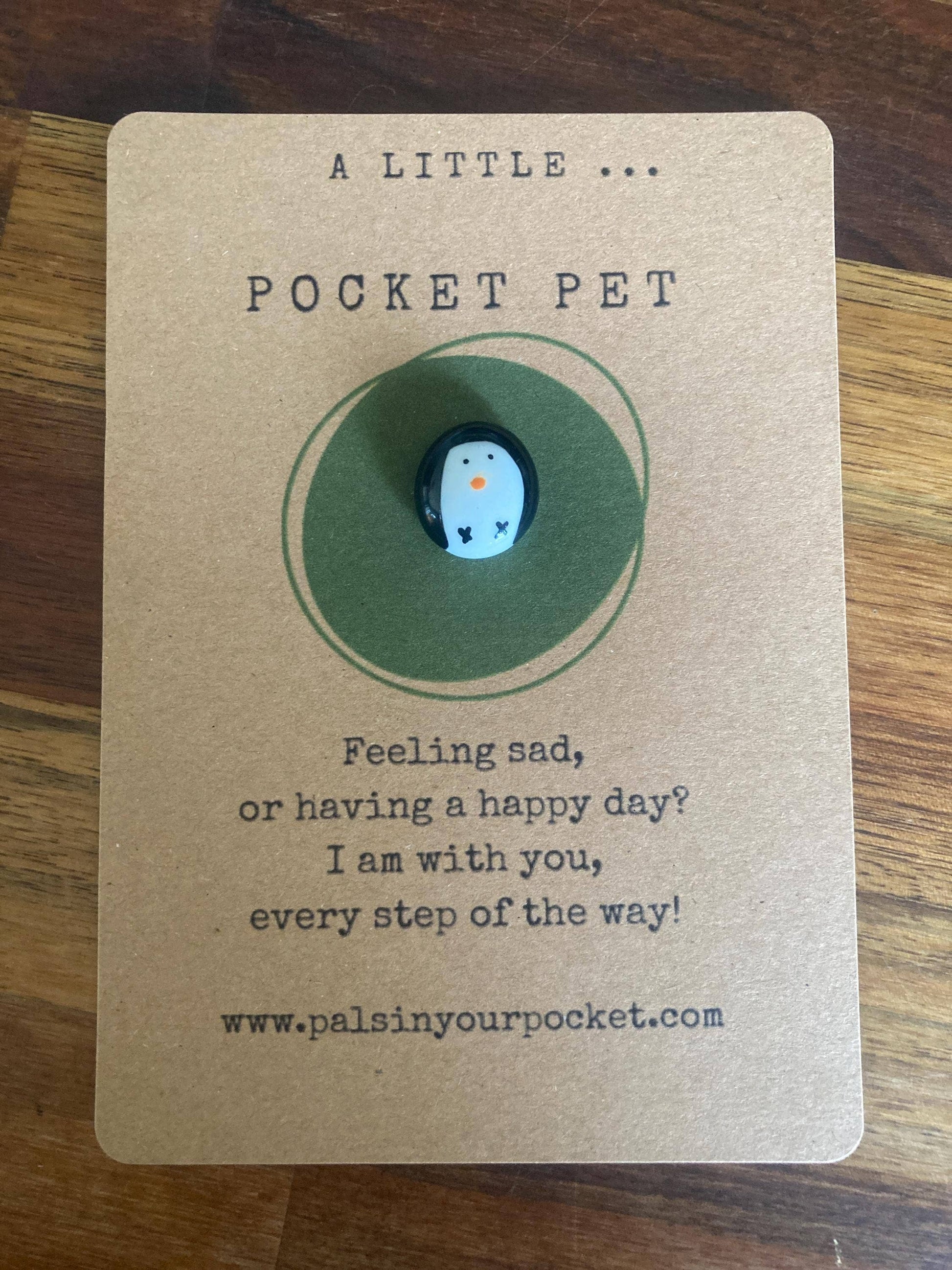 Small round white and black penguin charm on a brown card with text