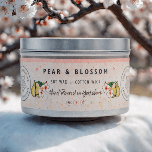 Candle in a tin with 'Pear & Blossom' label against a cherry blossom background