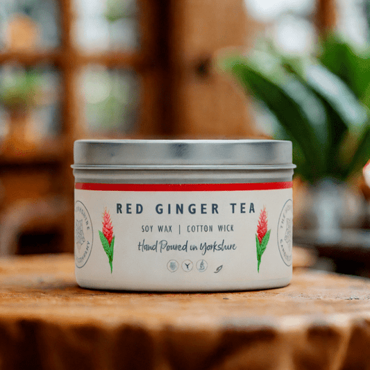 Candle in a tin labeled 'Red Ginger Tea' on a wooden surface with a blurred background