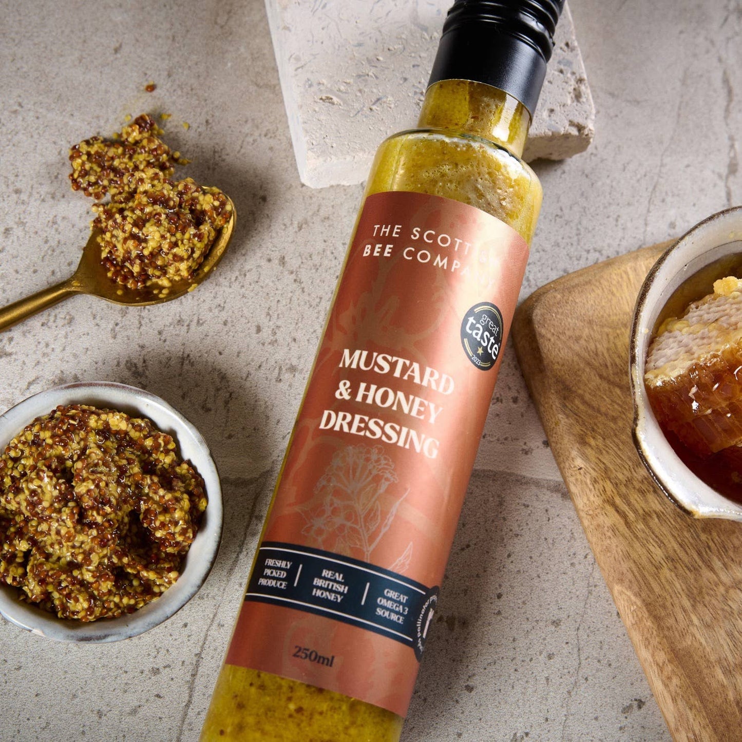 Close-up of Scottish Bee Company Mustard & Honey Dressing 250ml with mustard seeds and honey on wooden board