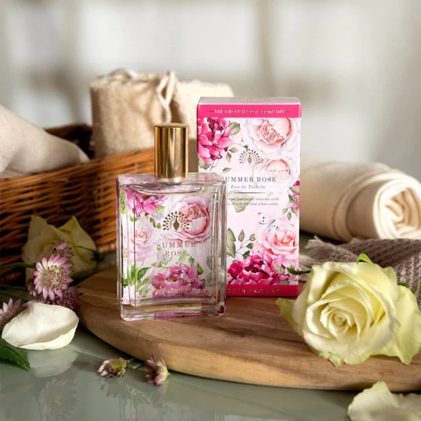 Floral perfume bottle and packaging on a wooden surface with flowers and towels in the background