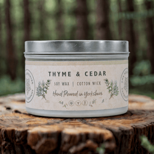 Candle in a tin labeled 'Thyme & Cedar' on a wooden surface with a natural background.
