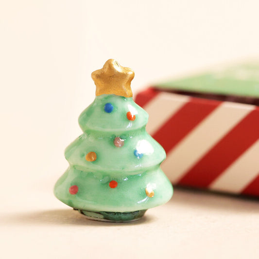 Small green Christmas tree figurine with a gold star on top, set against a blurred candy cane background.