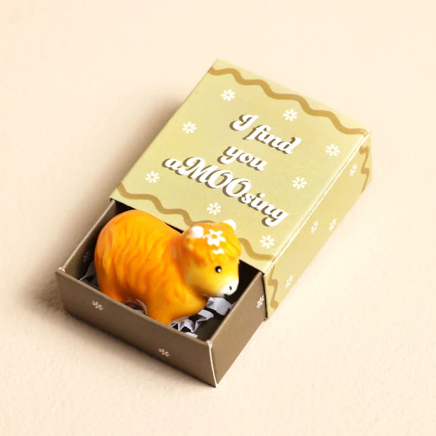 Close-up of the I Find You aMOOsing matchbox lid in sage green with gold wavy pattern