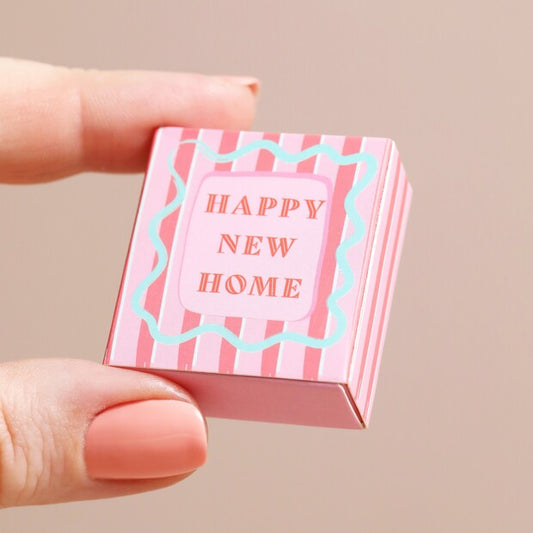 Small pink box with 'Happy New Home' text held by a hand against a beige background