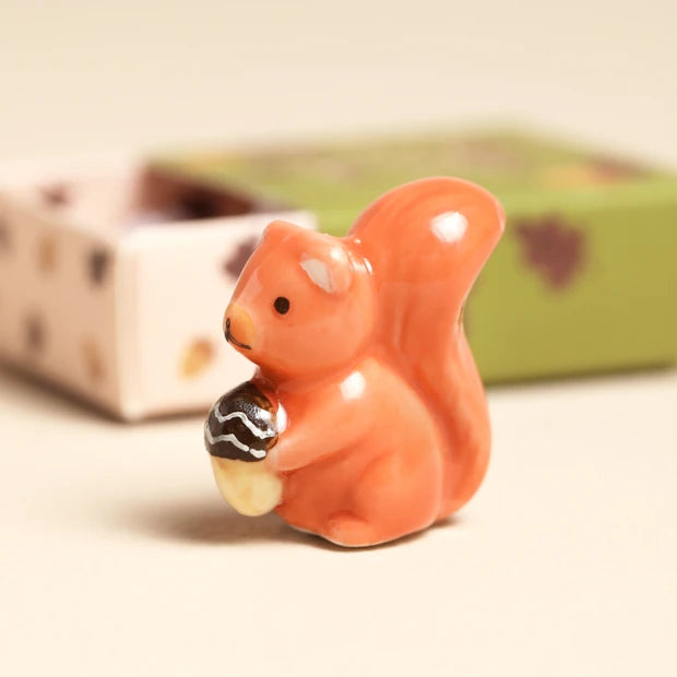 Tiny ceramic orange squirrel token holding an acorn with glossy glaze finish