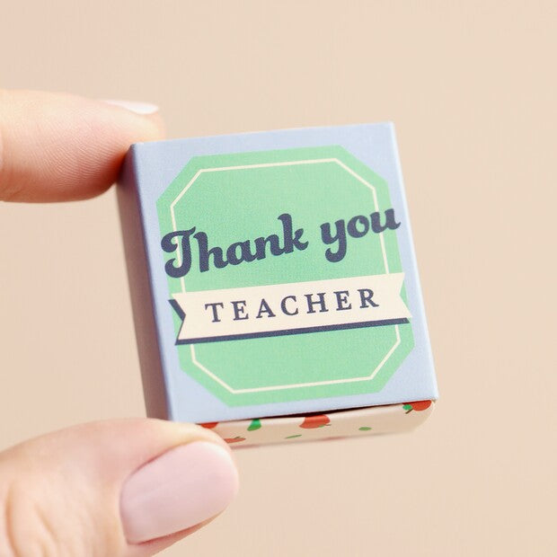 Small box with 'Thank you teacher' text held by a hand on a beige background