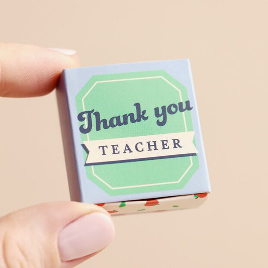 Small box with 'Thank you teacher' text held by a hand on a beige background