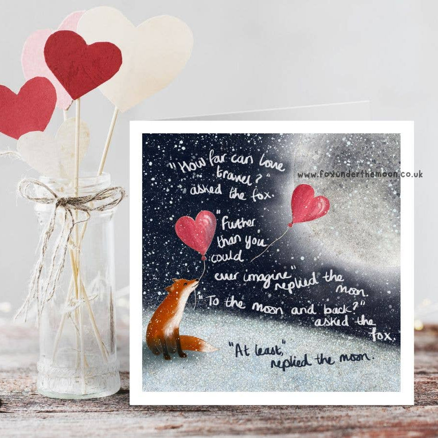 Card with fox and heart-shaped balloons next to a vase with heart-shaped objects on a wooden surface.